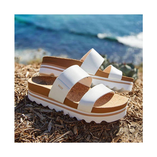 White platform sandals with cork footbeds and tan stripes, shown by the water