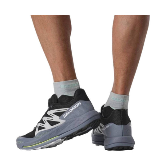 Black and gray trail running shoes with white side branding, shown on lower legs and heels