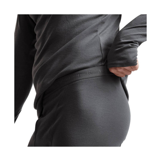 Dark gray merino base layer pants with a visible waistband logo and matching long-sleeve top at the waist