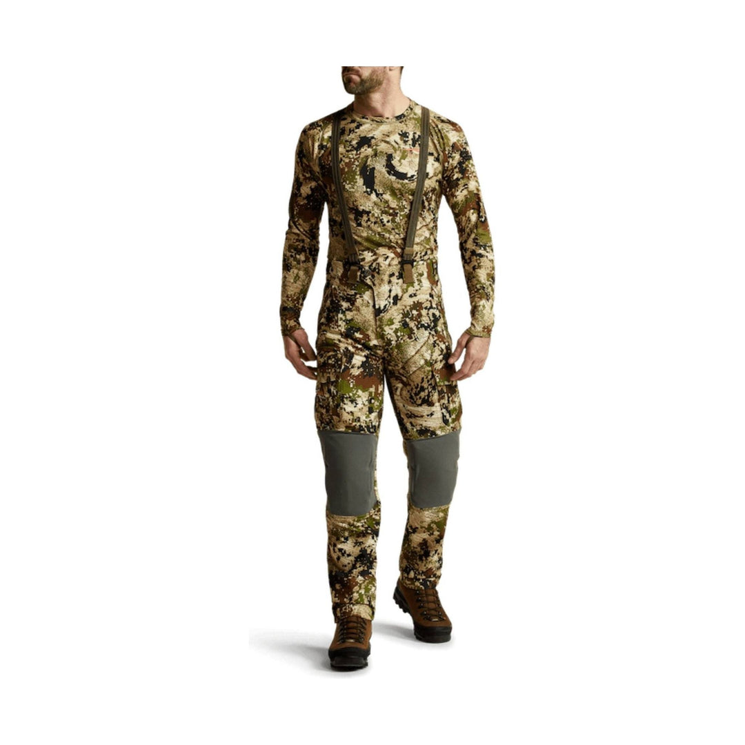 Camouflage hunting pants with built-in suspenders and gray knee panels, shown with brown hiking boots