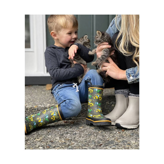 Taupe kids' rain boots with black soles worn by a child sitting beside an adult